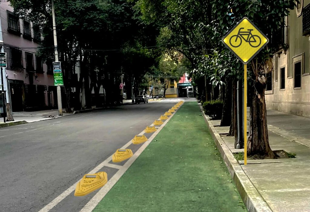 Ciclovía delimitada con canalizadores kayaks señalamiento vial amarillo de cruce ciclista en calle urbana arbolada, diseñada para mejorar la seguridad de los ciclistas.