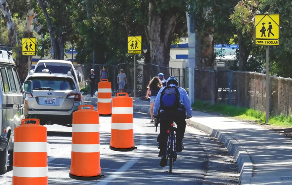 Zona escolar con ciclovía temporal delimitada por trafitambos naranjas y señalamientos amarillos de cruce peatonal, en una calle con alto flujo de estudiantes y ciclistas.