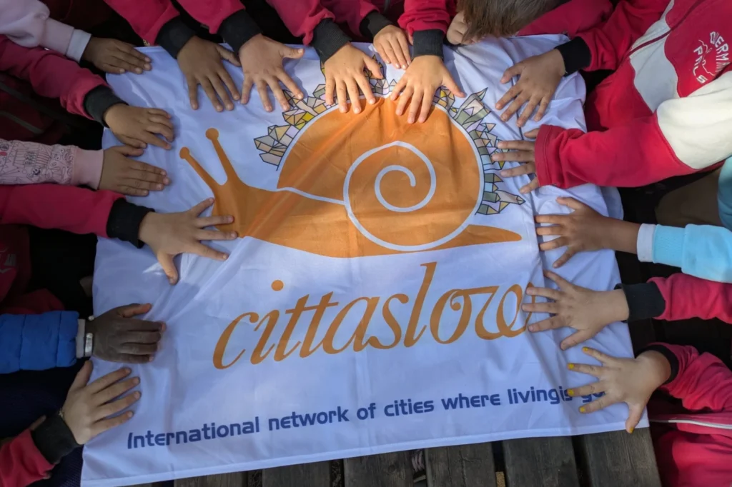Niños reunidos alrededor de la bandera oficial del movimiento Cittaslow durante una actividad comunitaria.
